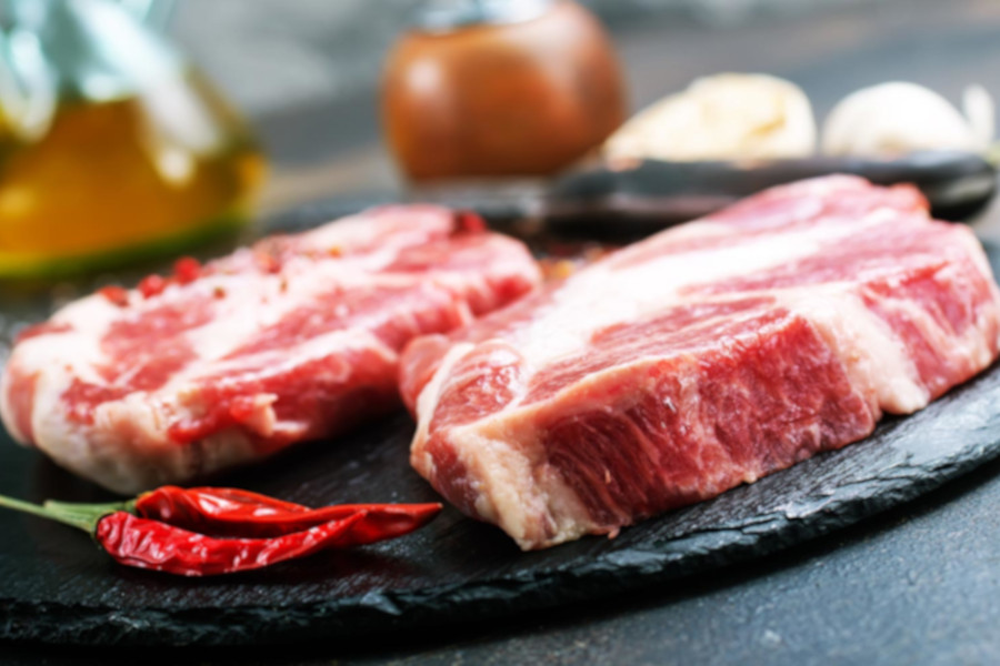 Zwei rohe Fleischstücke auf einer dunklen Platte, dekoriert mit Chili und Gewürzen